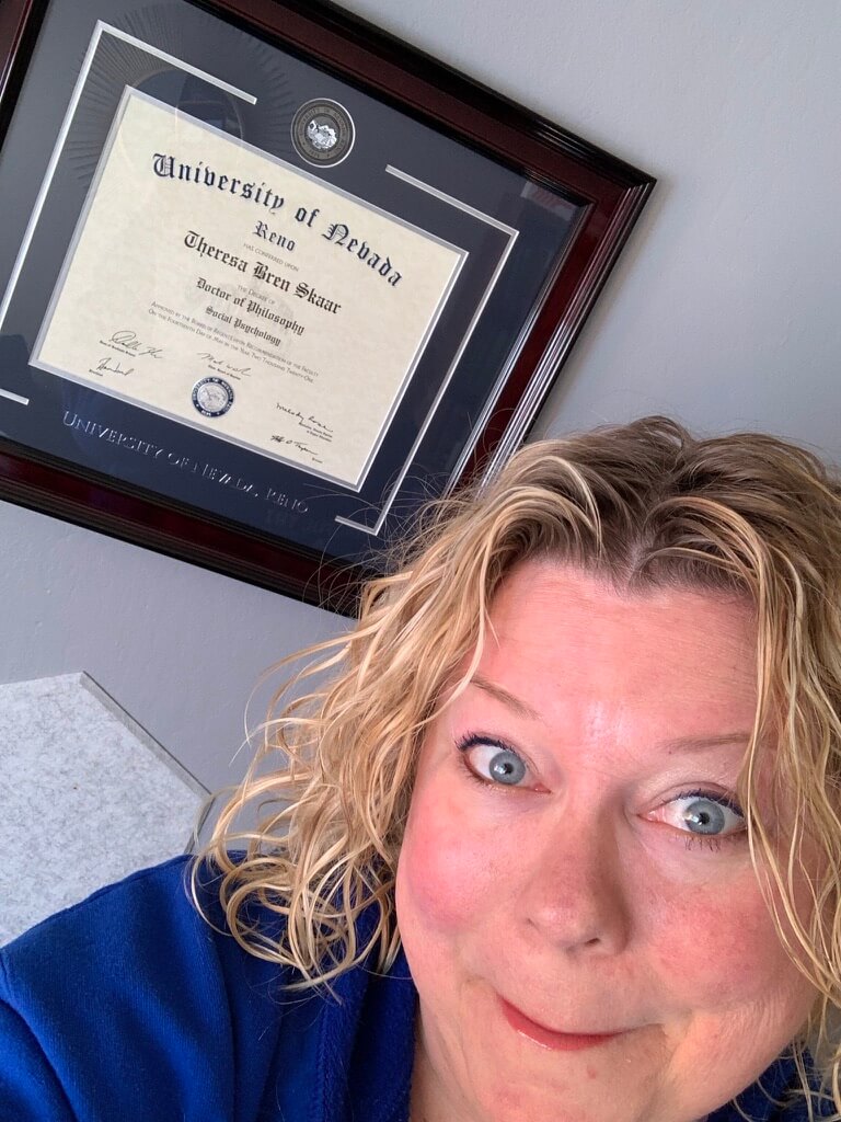 woman looking surprised in front of her graduate degree hanging on a wall behind her 